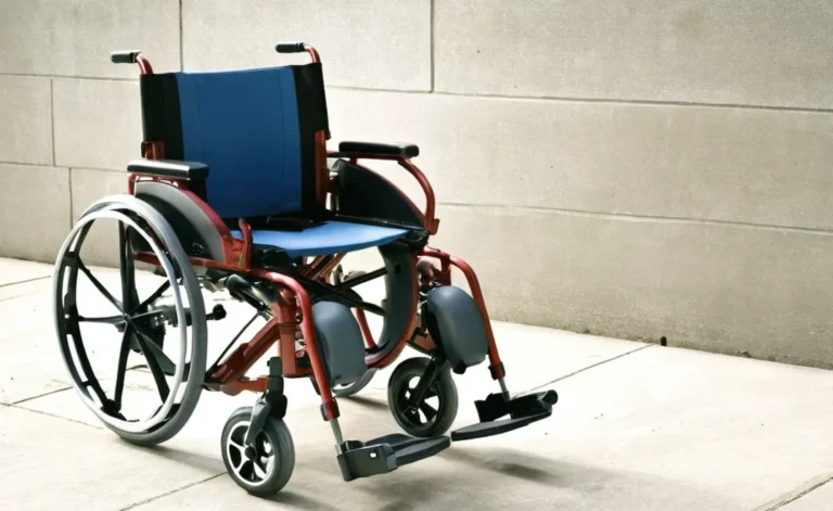 The Nitro Wheel Chair with red frame and blue leather is on the way having a wall in one side.